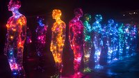 Luminous silhouettes of standing figures created with colorful LED lights glowing in vibrant neon colors against dark background, artistic light installation.