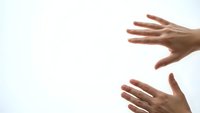 Two hands reaching toward each other against bright white background symbolizing connection, help, support and human interaction in minimalist style.