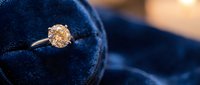 Elegant diamond engagement ring with sparkling solitaire stone on luxurious dark blue velvet jewelry box, romantic wedding proposal concept for couples.