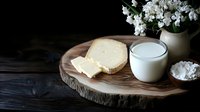 Fresh homemade cheese wheel with slices on rustic wooden board alongside glass of milk and cottage cheese for organic dairy product photography.