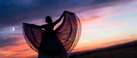 Woman dancing with flowing fabric against dramatic sunset sky, silhouette captures graceful movement and freedom, artistic expression in nature's colorful backdrop.