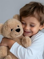 Smiling Caucasian boy hugging large beige teddy bear, wearing white long sleeve shirt against light gray background, expressing joy and childhood innocence.