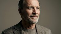 Middle-aged man with dark hair and full beard wearing casual beige sweater against neutral background, suitable for corporate, lifestyle, and professional portrait use.