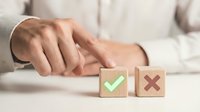 Professional businessman making decision between wooden blocks with green checkmark and red X symbols on desk in office environment.