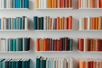 Colorful books arranged on white shelves, organized by color from blue to orange tones, creating a harmonious rainbow effect in a modern library.