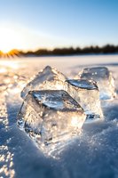 Transparent ice chunks on frozen lake surface catching golden sunlight at sunset, creating magical winter atmosphere with sparkling snow crystals and lens flare effects.