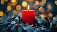 Red candle flame surrounded by eucalyptus leaves and red berries with golden bokeh lights creating festive holiday atmosphere for Christmas decoration.