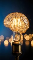 Glowing brain-shaped light bulb with warm filament against starry night sky background with bokeh lights representing creativity and innovation concepts.