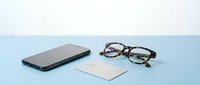 Smartphone, eyeglasses, and credit card arranged on a light blue surface, minimal flat lay composition for finance and technology concepts.