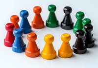 Colorful wooden game pieces arranged in curved formation on white surface. Classic board game pawns in red, blue, orange, yellow, green and black showing teamwork concept.