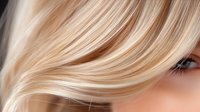 Close up of blonde hair strands flowing smoothly with soft highlights and natural shine, showing professional hair coloring and styling technique.