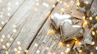 Rustic wooden heart decoration with warm golden fairy lights creating romantic ambiance on weathered wood background for Valentine's Day celebrations.
