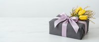 Elegant black gift box with purple ribbon and yellow tulips on white background for special occasions and celebrations.