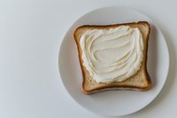 Fresh slice of white bread with creamy spread served on round ceramic plate against light background, minimalist food photography composition.