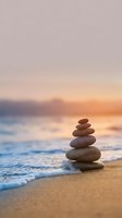 Zen stone stack on beach at sunset with gentle waves and warm golden light creating peaceful meditation atmosphere for wellness and mindfulness concepts.