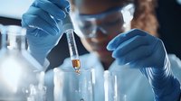Laboratory scientist in protective equipment conducting chemical analysis, pipetting liquid sample into test tube during scientific research experiment.