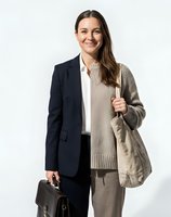 Professional businesswoman in navy blazer and beige sweater smiling confidently with handbag, isolated on white background for corporate design use.