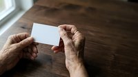 Close-up of senior male hands holding blank white business card over wooden table surface for branding and corporate identity mockup purposes.
