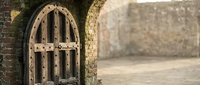 Ancient wooden arched door with metal hinges set in weathered stone wall, medieval architecture detail for historical and rustic design projects.