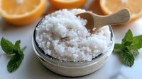 Fresh citrus body scrub with sea salt, orange slices and mint leaves on marble surface, natural skincare and spa treatment for exfoliation and aromatherapy.