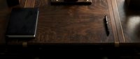 Executive workspace with dark wood desk, closed notebook, and pen in natural light for professional business settings.