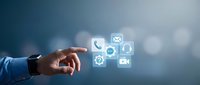 Business professional hand pointing at digital communication icons including phone, email, chat and video call symbols on blurred background for modern connectivity.