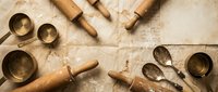Vintage wooden kitchen utensils and baking tools arranged on flour-dusted surface with handwritten recipe background for culinary design projects.