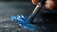 Artistic close-up of paintbrush with blue paint stroke on dark textured surface, showing creative process and artistic expression in macro photography.