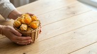 Close-up of hands holding wicker basket filled with fresh croissants on wooden table. Bakery product display for cafes, restaurants, food blogs, and culinary content.