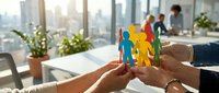 Diverse team members holding colorful paper cutout figures in modern office with city skyline, representing unity, collaboration, teamwork, and corporate diversity initiatives.