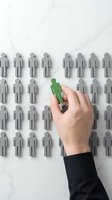 Hand holding green figure among gray figures on marble background, representing recruitment, hiring, talent selection, and human resources management for business concepts.