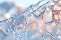Macro photography of soap bubbles creating abstract pattern with soft blue and peach tones, showing delicate transparent structures and light reflections.
