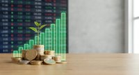 Sustainable finance growth concept with green plant sprouting from coins and rising bar chart against stock market data background on wooden desk.