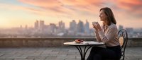 Young professional woman enjoying morning coffee on urban rooftop terrace with city skyline view during golden hour sunrise for lifestyle and business concepts.