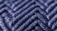Detailed macro view of navy blue knitted wool fabric texture showing diagonal pattern and yarn fibers. Warm winter clothing material background with soft focus.