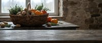 Woven basket filled with fresh vegetables and herbs displayed on rustic wooden table near window, suitable for food styling and autumn harvest themes.