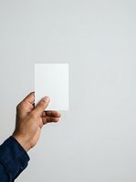 Male hand with dark skin tone holding blank white card against neutral background, wearing dark blue sleeve. Suitable for business branding, identity mockups, and promotional campaigns.
