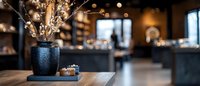 Cozy cafe interior with decorative vase and dried branches on wooden table, warm lighting and blurred restaurant background for hospitality design.