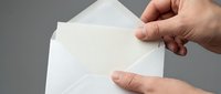 Hand holding white envelope with blank letter paper emerging from opening against gray background for business correspondence and mailing concepts.