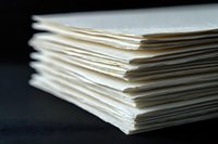 Stack of white paper sheets with layered edges against dark background, selective focus on textured paper pile creates minimalist office composition.