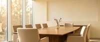 Modern conference room with wooden table and beige chairs in bright office space with large windows and natural lighting for business meetings.