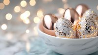 Speckled rose gold Easter eggs in marble bowl against soft bokeh lights background. Elegant holiday decor with metallic and white color scheme creates festive atmosphere.