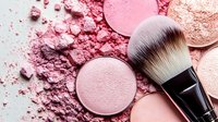 Pink and coral makeup powder palette with professional brush scattered cosmetic dust beauty products for application and blending techniques.