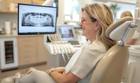 Middle-aged female patient viewing dental x-ray results on monitor while seated in comfortable dental chair during consultation in modern dental office.