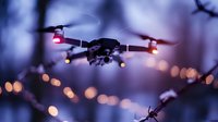 Drone with glowing navigation lights flying at dusk against blurred bokeh city lights background, creating atmospheric aerial photography scene.