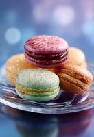 Colorful French macarons in pastel shades of pink, mint green and orange arranged on glass plate with soft bokeh background, close-up view of delicate meringue cookies.