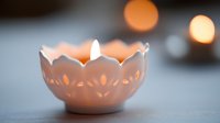 Glowing ceramic candle holder with delicate floral cutout pattern creates soft ambient lighting against blurred background, capturing serene atmosphere.