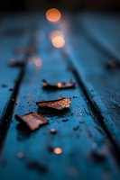 Fallen autumn leaves on wet blue wooden surface with golden bokeh lights creating dreamy atmosphere. Macro photography with shallow depth of field.
