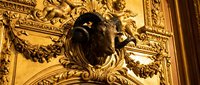 Ornate golden ceiling detail with carved lion head sculpture and decorative baroque molding in luxury interior architecture.