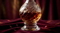 Crystal whiskey decanter filled with amber bourbon on elegant burgundy velvet surface with warm golden lighting creating luxury bar atmosphere.